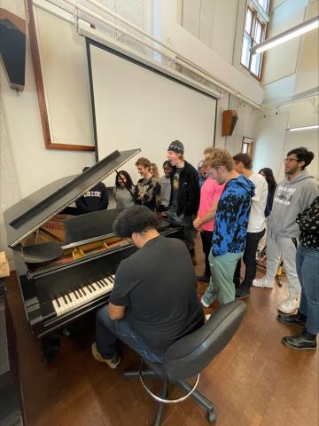 group of students surrounding an instructor at the piano