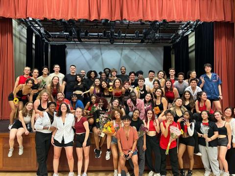 Photo of the members of Evolution dance group on a stage, many holding flowers