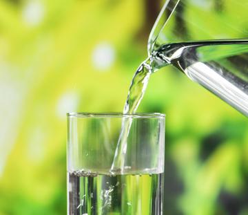 Close up photograph of water being poured from a pitcher into a glass.