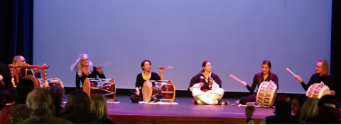 A group of performers seated on a stage playing various Korean drums
