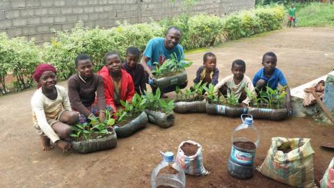 Tabi Joda sitting with a group of children, each holding a small tree seedling.