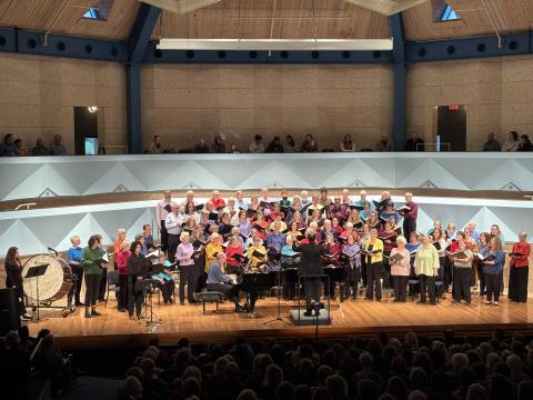 The Middlebury College Community Chorus, dressed in vibrant colors, sings on the stage in Robison Hall.