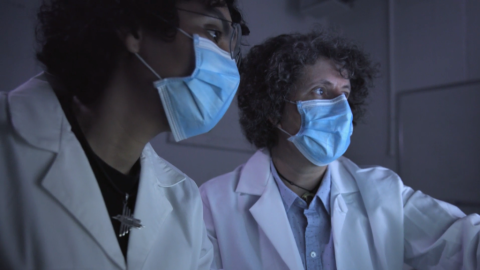 Two people in lab coats and simple face masks covering mouth and nose.