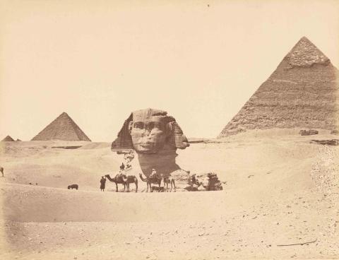 Desert image with pyramids in the background and camels and riders in the foreground