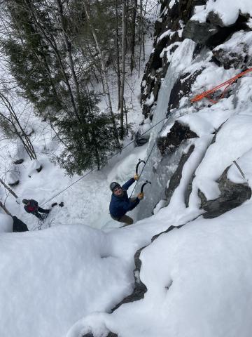 Student looking on the camera ice climbing, with snow in the background.