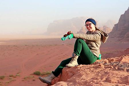 Photo of a student sitting on a rock outcrop, overlooking the desert of Wadi Rum.