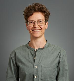 Woman with short brown hair, glasses, smiling. Wearing green shirt.