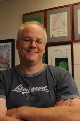Person with glasses in grey t-shirt and arms folded in front.
