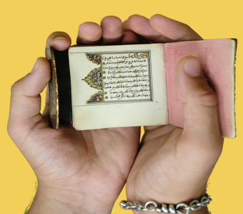 hands holding an illuminated manuscript with a yellow background