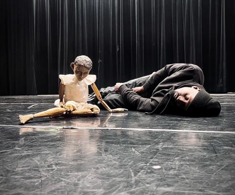 dancer laying on stage next to a puppet