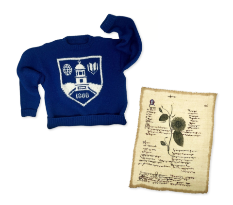 blue knit sweater with middlebury shielf and embroidered textile rectangle resembling a sheet of paper