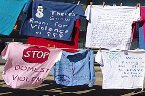 A picture of hand-painted t-shirts handing on clotheslines. The t-shirts urge an end to violence.