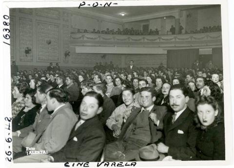 Historic black and white image of a theater audience dressed in formal attire.