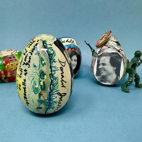 four wooden eggs decorated with ink, collage, and 3-D objects, and signed on a blue background