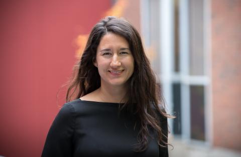 Woman with long dark hair, black shirt. Soft rose background with windows.
