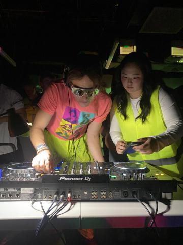 two students in dayglo yellow at a DJ turntable