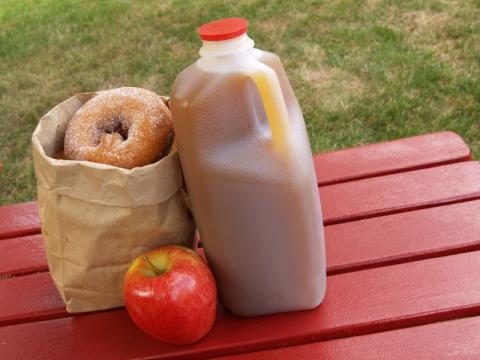 bag of cider donuts with cider jug and one red apple on red table
