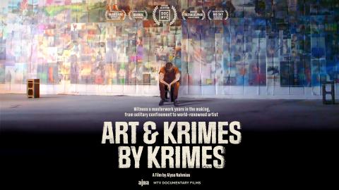Wide angle photograph of a figure in a red jump suit in front of a wall display of his work of faded faces and locations.
