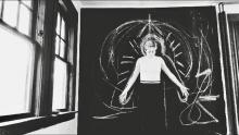black and white photo of a person standing against a chalkboard, looking down, with arms extended out