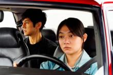 Woman driving a car with a man in the backseat, looking out of the window