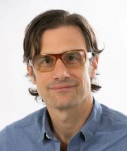 Picture of a man with brown hair and glasses wearing a blue shirt