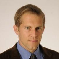 Man with light brown hair wearing a tie and light blue shirt