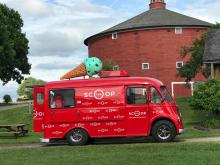 Red ice cream truck with an ice cream cone of the top in front of a red round barn