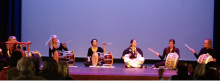 A group of performers seated on a stage playing various Korean drums