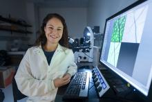 Woman in white lab jacket standing in from of large computer screen.