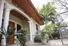 building entryway with white pillars on either side of a wooden door, potted plants, fence and trees in the background