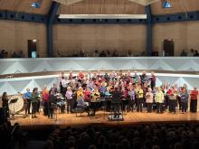 The Middlebury College Community Chorus, dressed in vibrant colors, sings on the stage in Robison Hall.