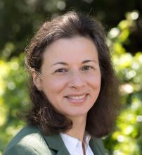 Woman smiling with greenery in the background.