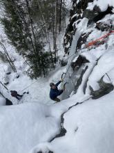 Student looking on the camera ice climbing, with snow in the background.