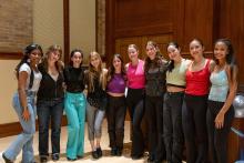 Ten girls with arms around each other, posing at the edge of the stage after tap performance.