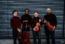 the artists standing in front of a wall holding their instruments