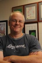 Person with glasses in grey t-shirt and arms folded in front.