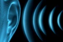 Large blue ear with blue curved lines depicting sound waves moving towards the ear on a black background.