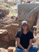 Savage sitting in dirt in front of a large stone