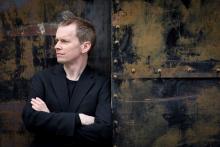 The artist in profile, leaning against a wall with his arms crossed