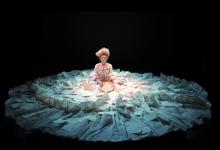 actor sitting in the spotlight on a dark stage