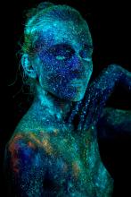 A nude woman in the dark dotted with fluorescent paint that is illuminated.