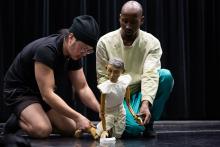 two dancers kneeling on stage with a puppet