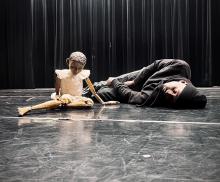 dancer laying on stage next to a puppet
