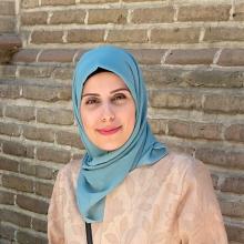 smiling light-skinned woman wearing an aqua headscarf and beige jacket