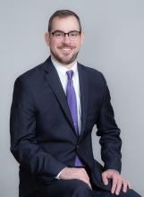 photo of Mike Castiglioni '11 seated, wearing glasses, purple tie, navy blue suit.
