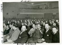 Historic black and white image of a theater audience dressed in formal attire.