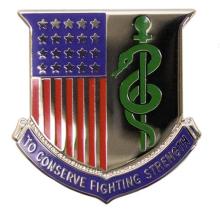 A silver shield with a representation of the national flag on the left side of the shield. On the right of the shield is the symbol of medicine, the Staff of Aesculapius, a rod wrapped by a single serpent.