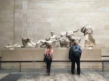 Two people look at a series of classical sculptures