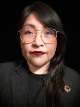 Head shot of Alina Duarte wearing glasses, a black shirt, and a black blazer.
