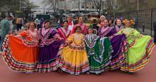 Eleven Mexican dancers pose outside in highly colorful costumes